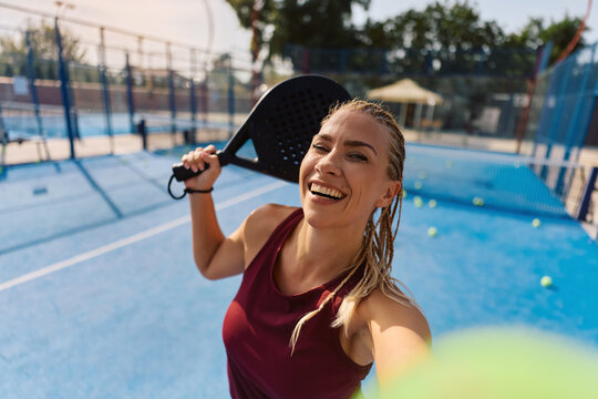 Happy sportswoman taking selfie while playing paddle tennis and looking at camera.