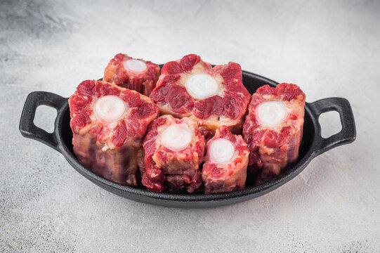 Raw beef oxtail pieces in cast iron skillet with thyme and rock salt, top view butcher style preparation for slow cooking