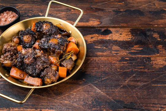 Homemade beef oxtail ragout in pan, gelatin rich slow cooked meat with vegetables in dark sauce, overhead shot
