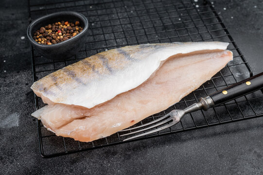Raw pike perch fillets on dark background, one skin-on and one skinless, fresh freshwater white fish meat ready for cooking.