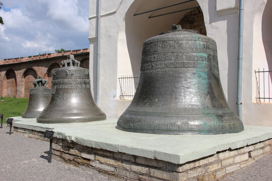 Ancient bronze church bells with traditional ornate inscriptions and decorations displayed outdoors on a pedestal in the Novgorod Kremlin