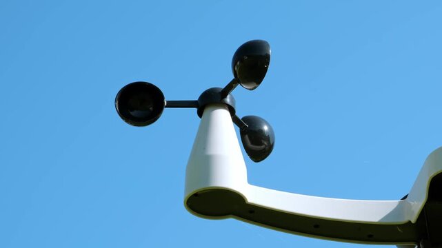 An anemometer measuring wind speed outdoors on blue sky background. Weather monitoring, meteorological equipment, climate study. Modern wireless weather station. Smart home technology. HQ 4K.