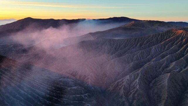 Steam drifts through rugged, volcanic valleys at dawn. Soft light bathes dark ridges at Bromo