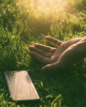 Hand touching fresh green grass beside smartphone lying face down, touch grass and reconnect with nature concept