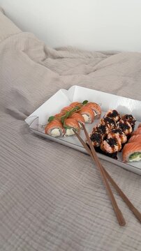Sushi set of 3 rolls in paper packaging with wooden sticks laying down on the bed at home. Sushi asian food delivery to home, japanese cuisine, philadelphia roll and felix roll with salmon