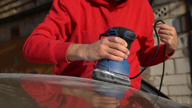 Horizontal video of a man polishing a car body with a rotary buffer machine. Professional auto detailing and paint restoration process.