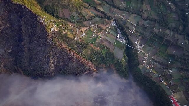 Clouds drift below steep cliffs. Fields and houses nestle in valley embrace at Bromo