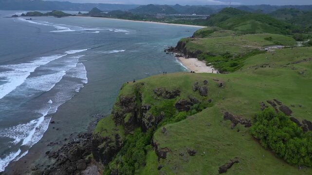 Wide Drone Shot Rugged Coastline And Ocean Under Moody Sky Deep Blue Water, Crashing Waves On Basalt Cliffs, Distant Islets, Group of Tourists, Bukit Merese, Lombok, Tanjung Ann