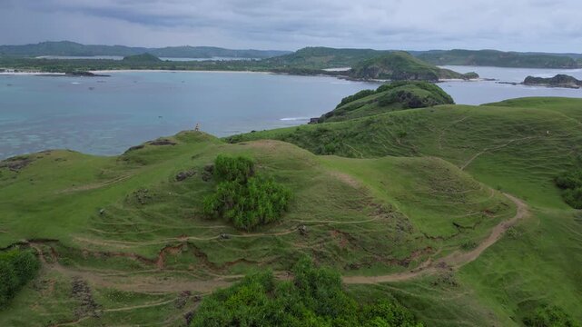 Group Hikers Traversing Windswept Coastal Ridge Above Surf And Sandy Coves, Cinematic Aerial Perspective Shows Winding Trails, Lush Green Headlands, Energetic Trek With Panoramic, Lombok