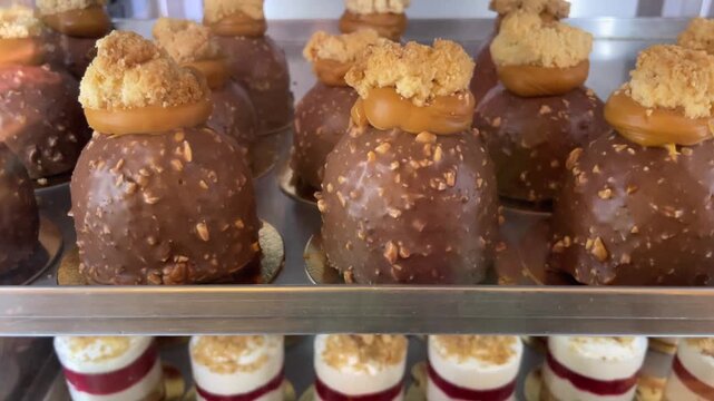 Pastries for sale. Refrigerated pastry display featuring chocolate coated dome pastries on upper shelf and mini layered cheesecakes on lower shelf. 