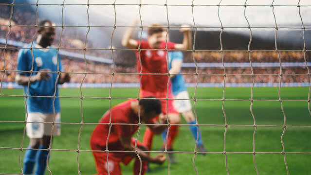 Red team players score a winning soccer goal as the goalkeeper misses the save, capturing attacking action, defeat and match competition on the pitch.