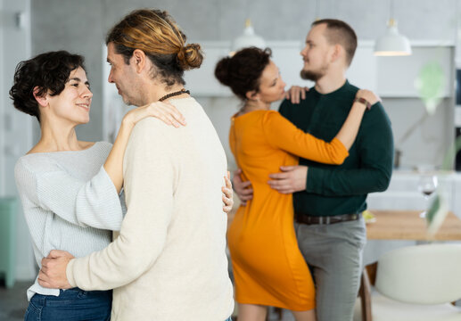 Four adult friends dancing and singing at home. Cheerful women and men enjoy music together. Happy party people celebrating friendship