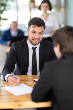 Male bank employee advises a client against the background of the office interior. In a modern bank, the consultant offers the client a favorable mortgage rate