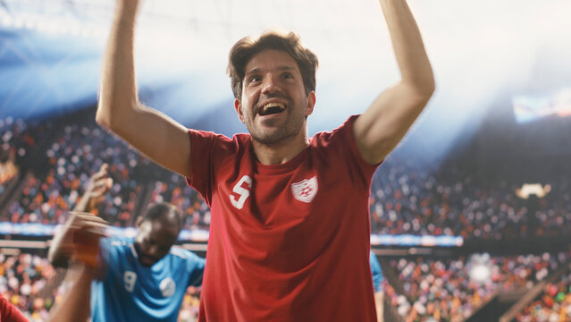 Diverse football players celebrate a winning goal with raised arms and clenched fists while devastated opponents react before cheering fans.