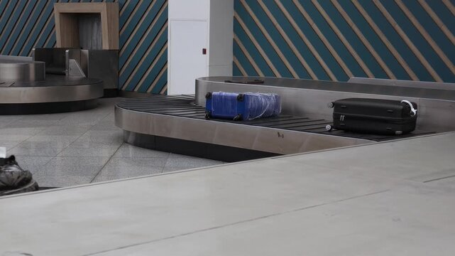 Various luggage bags move along metal baggage carousel conveyor belt inside airport terminal hall.