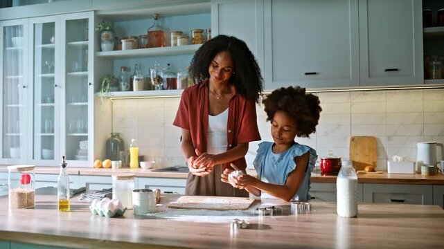 Mom daughter shaping dough kitchen counter. Happy multiracial family baking.