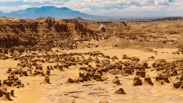 A low aerial view (facing south) inside the Valley of the Goblins of Goblin Valley State Park, Utah. A dried up creek bed meanders downhill through the sand and clay.