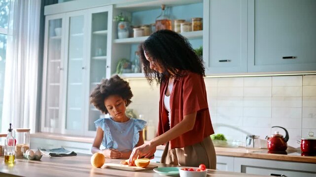 Mother slicing orange kitchen counter. Daughter watching mom cutting fruit home.