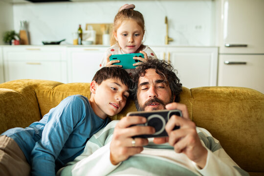 Father playing mobile game with kids on sofa at home