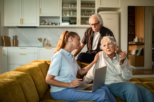 Caregiver helps concerned senior woman at home with laptop