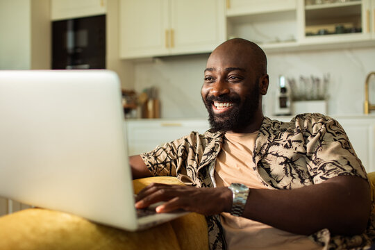 Smiling man typing on laptop in home kitchen