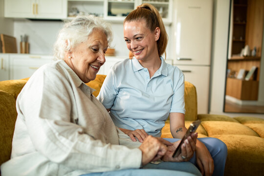 Home caregiver teaching senior woman to use smartphone
