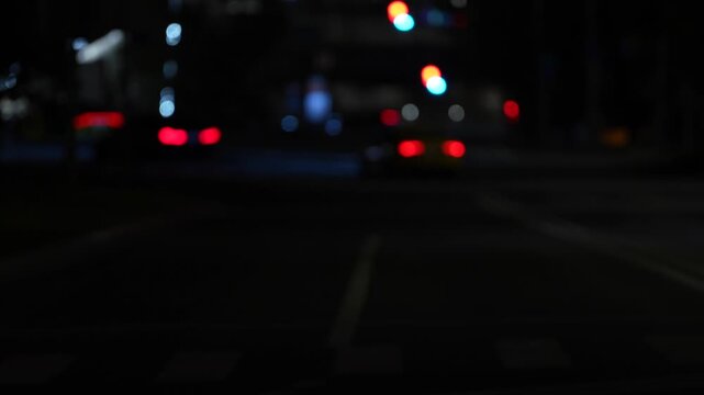 Intentionally defocused night traffic with glowing car taillights and distant city lights on a dark urban road, creating an atmospheric bokeh background representing transportation, night driving and 