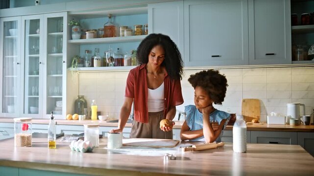 Baking cookies home kitchen. Mother kneading dough daughter watching curious.