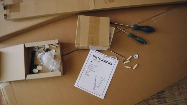 Top view on unpacked flat pack furniture with a complete set of assembly parts, essential tools like screwdrivers, and detailed DIY instruction manual lying on large cardboard boxes ready for assembly