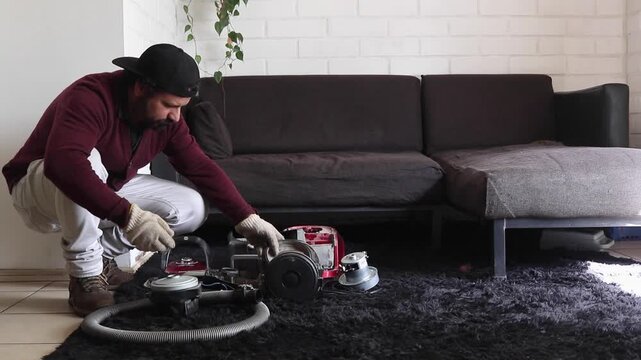 Handyman crouching on rug inspecting disassembled vacuum cleaner parts at home