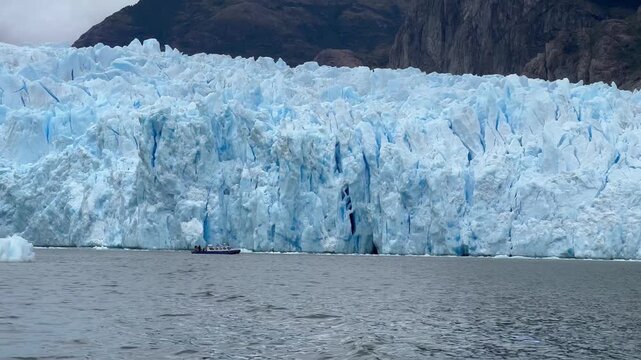 Small tourist boat sails along a large glacier drop, seracs and glacial ice, Glaciar San Rafael glacier lagoon at Golfo Elefante glacier lagoon, Ays&eacute;n, Chile