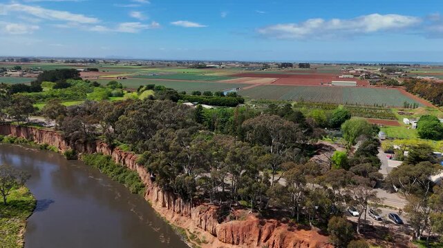 Aerial drone view along Werribee River at Werribee South, Melbourne, Victoria, Australia, with a steep eroded red-orange cliff face above Werribee River, eucalyptus trees and bushland along the edge.