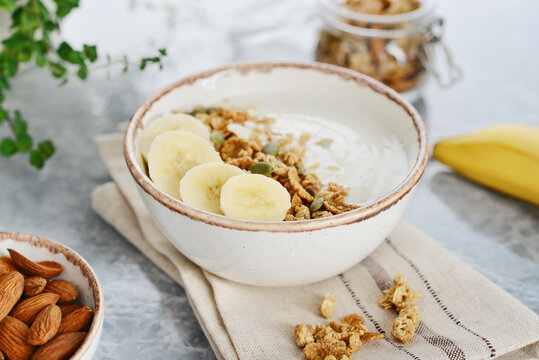 Greek yogurt with muesli and sliced banana in a bowl on a marble countertop