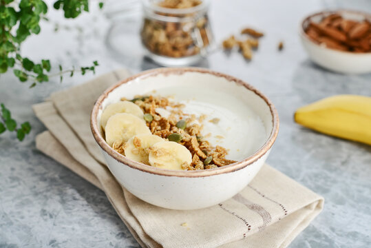 Greek yogurt with muesli and sliced banana in a bowl on a marble countertop
