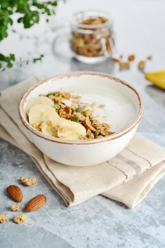 Greek yogurt with muesli and sliced banana in a bowl on a marble countertop