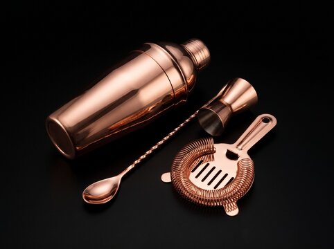 Copper barware tools including a shaker and strainer on a black