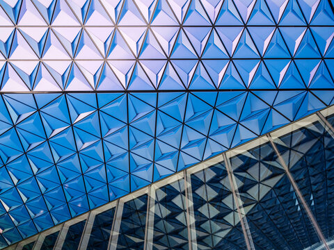 Close-up of a triangulated glass and metal roof structure with repeating pyramidal panels, transitioning from pale white at top to deep blue below. 