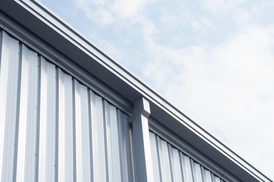Corrugated metal siding facade and roof gutter system on modern industrial warehouse against cloudy sky. Metal building construction, industrial roofing, drainage and architectural siding concept.