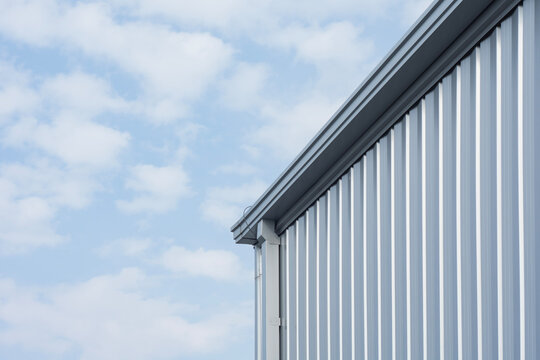 Corrugated metal siding facade and roof gutter system on modern industrial warehouse against cloudy sky. Metal building construction, industrial roofing, drainage and architectural siding concept.