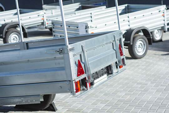 Open galvanized steel utility car trailers parked outdoors in row on paved lot. Cargo transport equipment, commercial vehicle towing, freight hauling and logistics trailer rental concept.