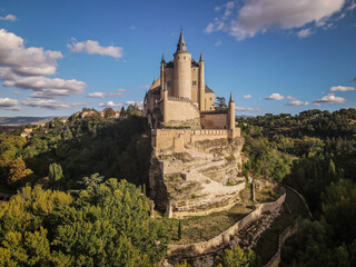 Alcázar of Segovia castle stands on a rocky outcrop surrounded by lush trees © Greggory Zzyzx