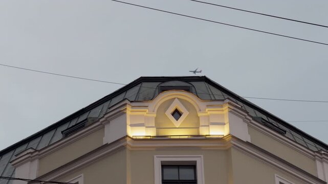 Illuminated historic building facade with roof peak and power lines against overcast sky