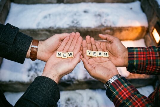 Two pairs of open hands holding NEW YEAR letter tiles over snowy steps, representing a fresh start
