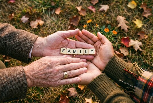 Multigenerational hands layered over FAMILY letter tiles on autumn grass, symbol of generations