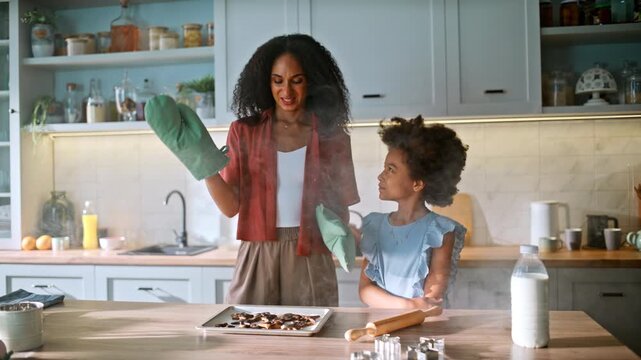 Mother daughter upset over smoking burnt cookies tray. Baking fail home kitchen.