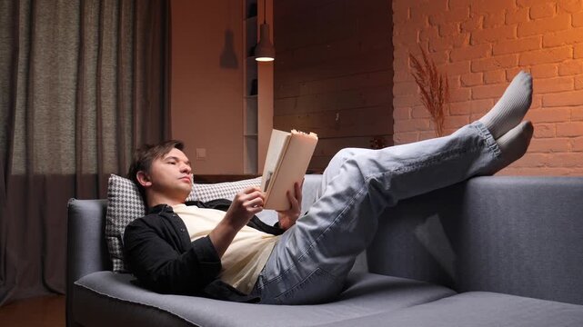 Man enjoying leisure time, reclining comfortably on a couch in the living room, reading a book in the soft evening light, finding solace and peace at home