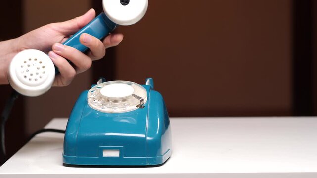 Person's hand lifting the receiver of a classic turquoise rotary telephone, engaging in communication and connecting with others using retro technology