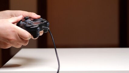 Person holding a black wired video game controller, actively pressing buttons and controlling joysticks, engaging in electronic entertainment on a white surface © Aliaksandr