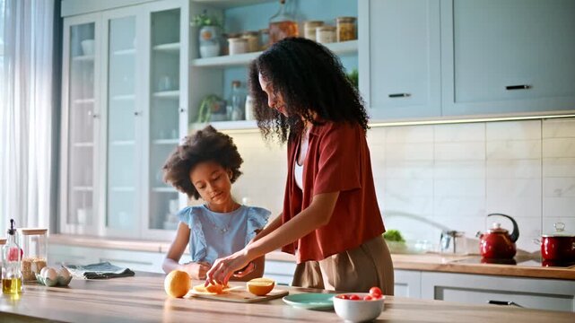 Daughter cutting orange kitchen mom teaching. African american family cooking.