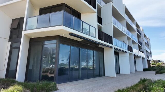 Slow motion of a modern apartment building in Australia, with a vacant glass shopfront at ground level and residential apartments with balconies on the upper floors. Commercial property, real estate.